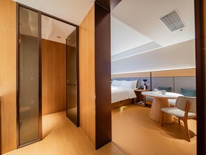 A modern hotel room with a bed, bedside table, chair, and a glass-enclosed shower area. - JI Hotel (Xi'an)