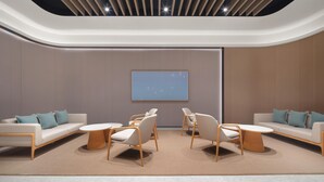 Un interior moderno con techo curvo, iluminación empotrada, una zona de estar central con sofás y sillones, y una pieza de arte minimalista en la pared.