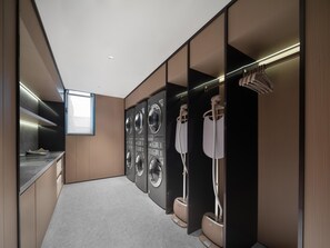 A modern laundry room with built-in washers and dryers, a countertop with a sink, and a window providing natural light. - JI Hotel (Xi'an)