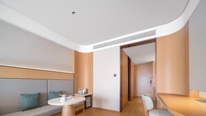 Una habitación de hotel moderna con sofá, una mesa redonda, un escritorio y una silla.