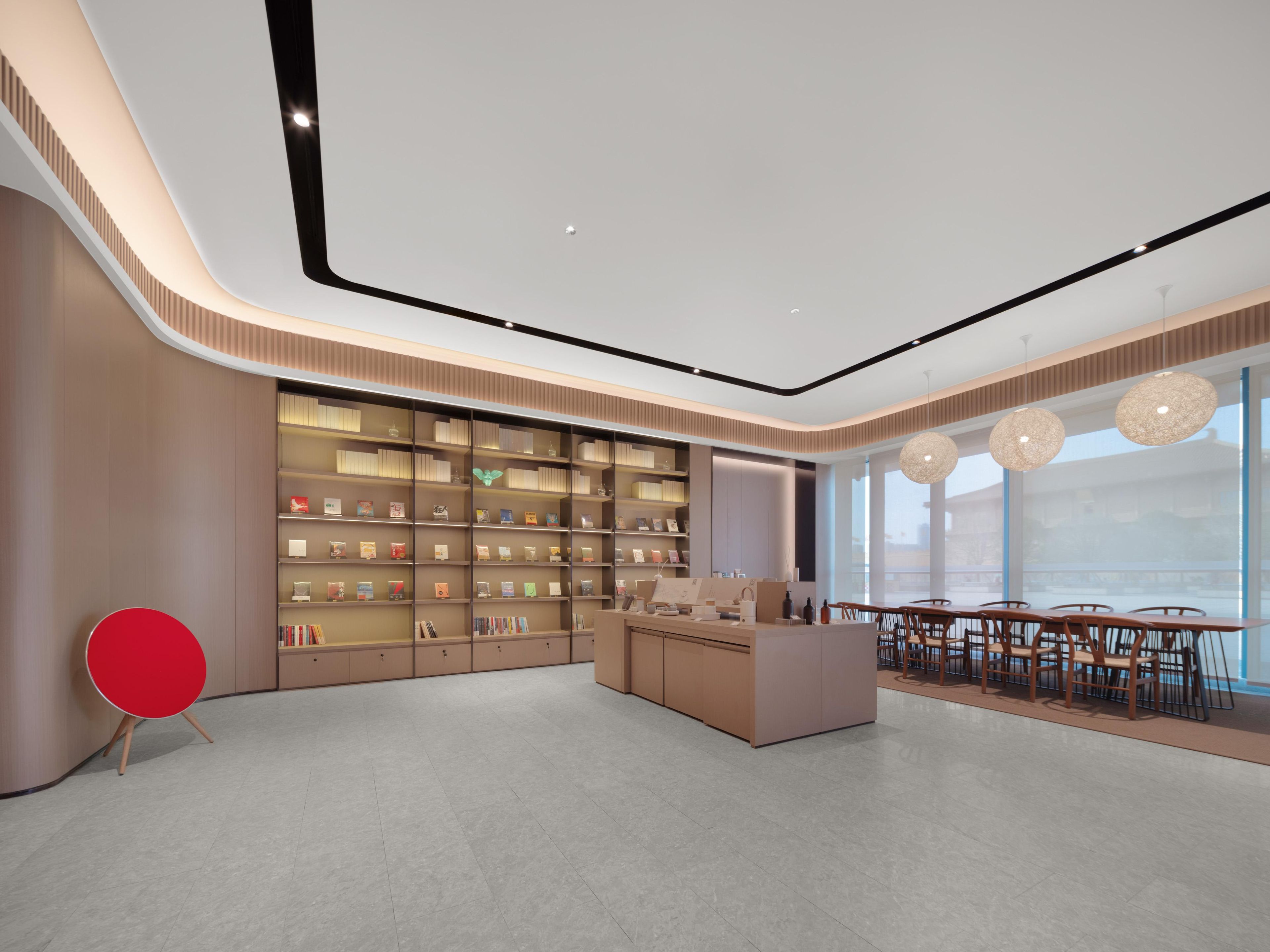 A modern interior with a central reception desk, a large bookshelf, and a dining area with tables and chairs.