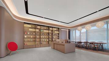 A modern interior with a central reception desk, a large bookshelf, and a dining area with tables and chairs.