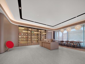 Um interior moderno com uma receção central, uma grande estante de livros e uma área de refeições com mesas e cadeiras.