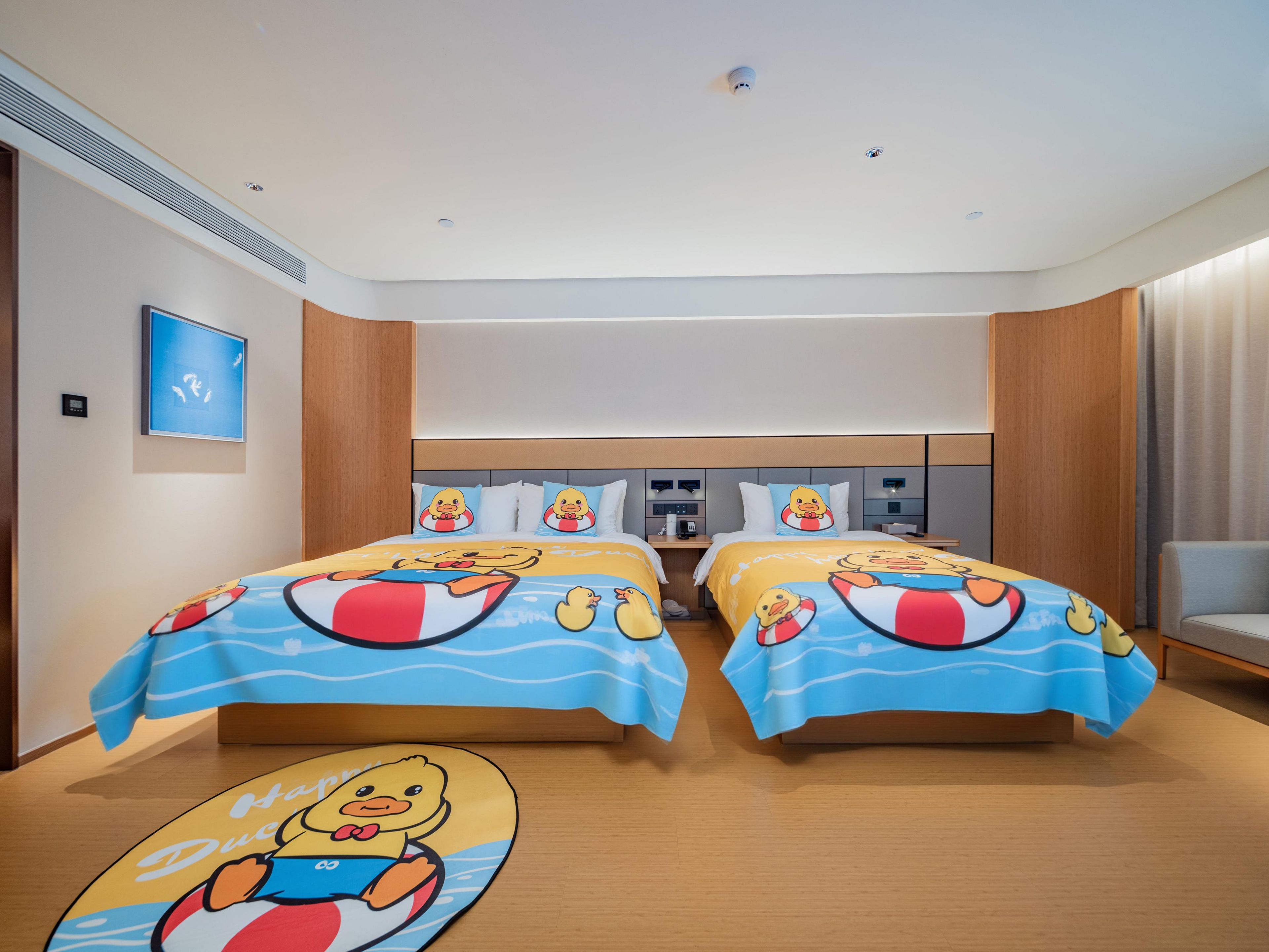 A hotel room with two beds, each with a duck-themed bedspread, a small table, a chair, and a wall-mounted control panel.