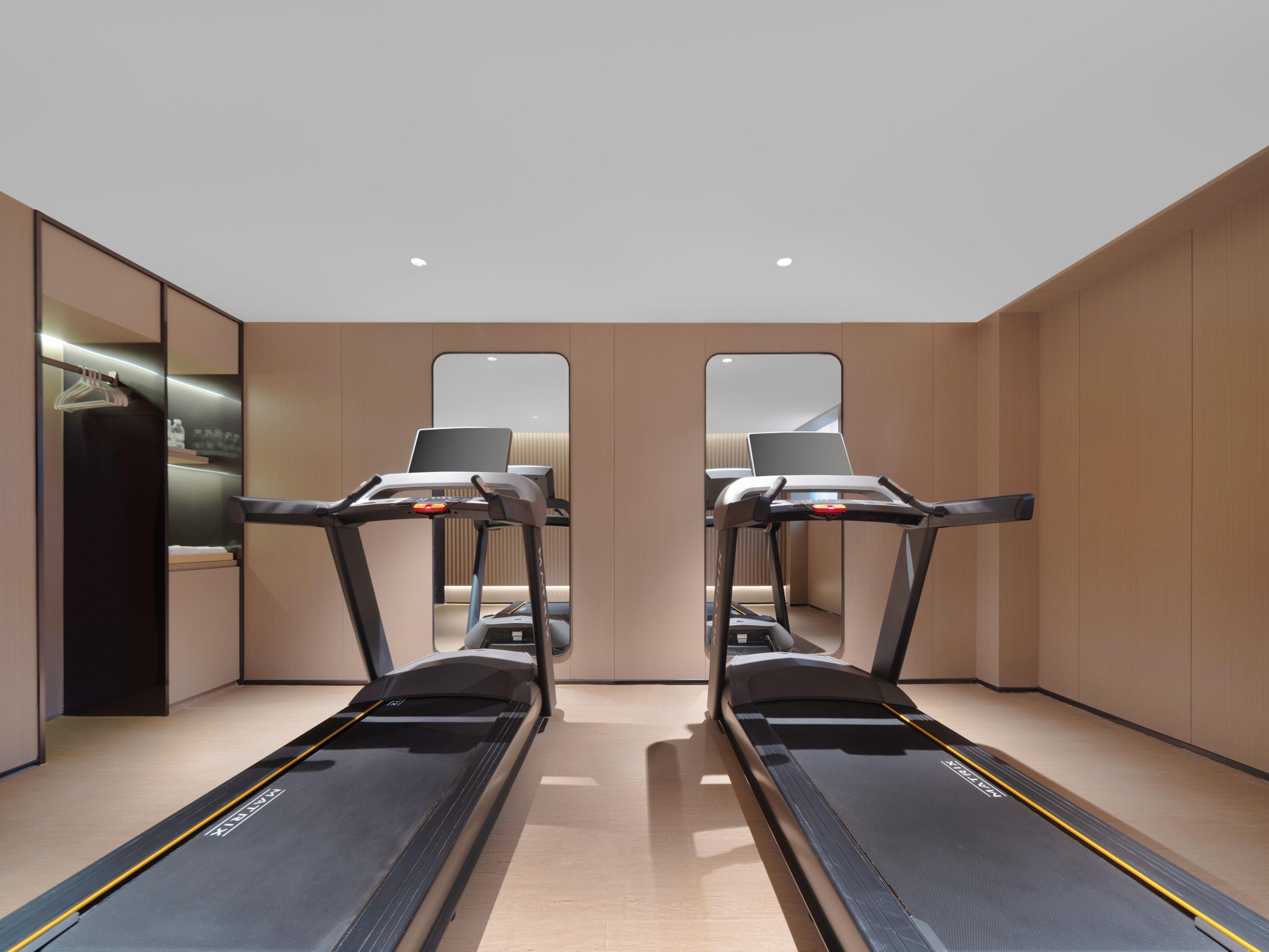 A modern room with two treadmills, a mirror, and a laptop on each treadmill.