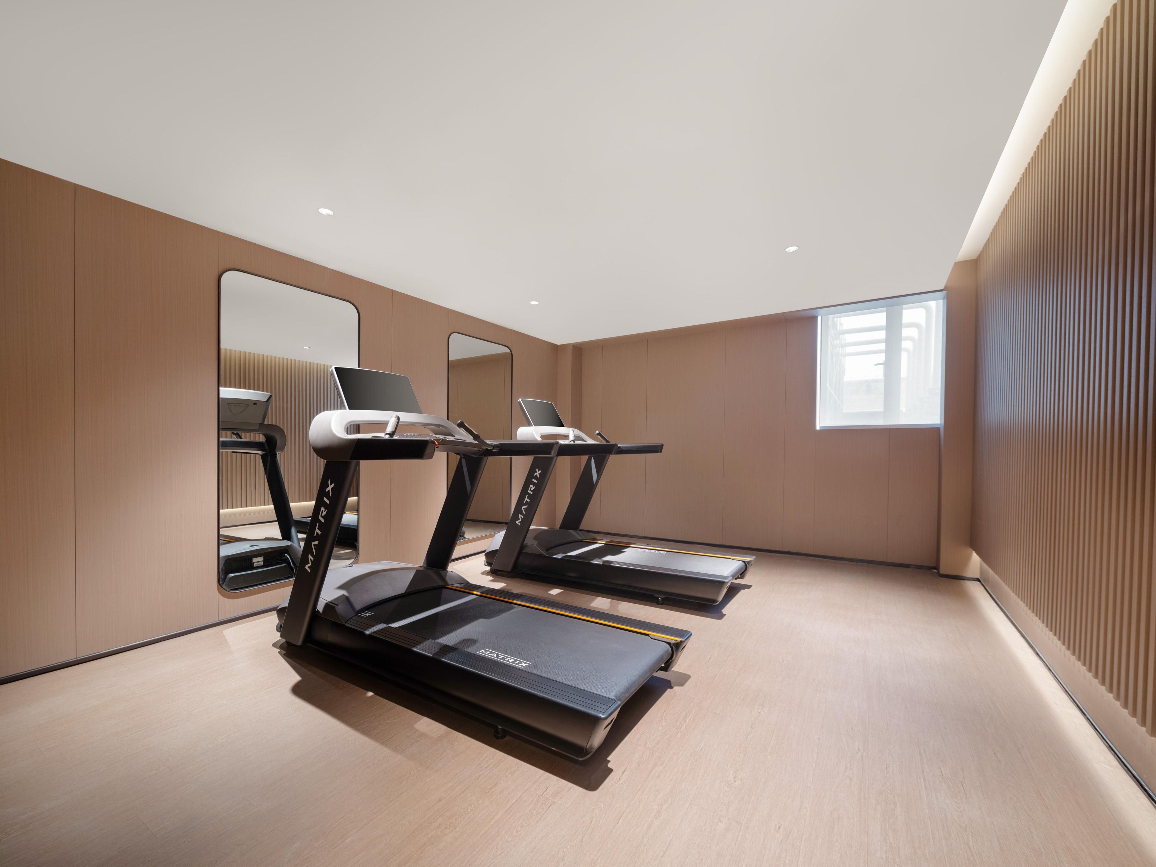 A modern gym with treadmills, a mirrored wall, and a large window.
