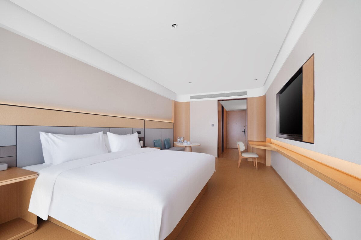 A modern hotel room with a large bed, bedside tables, a desk, and a TV.