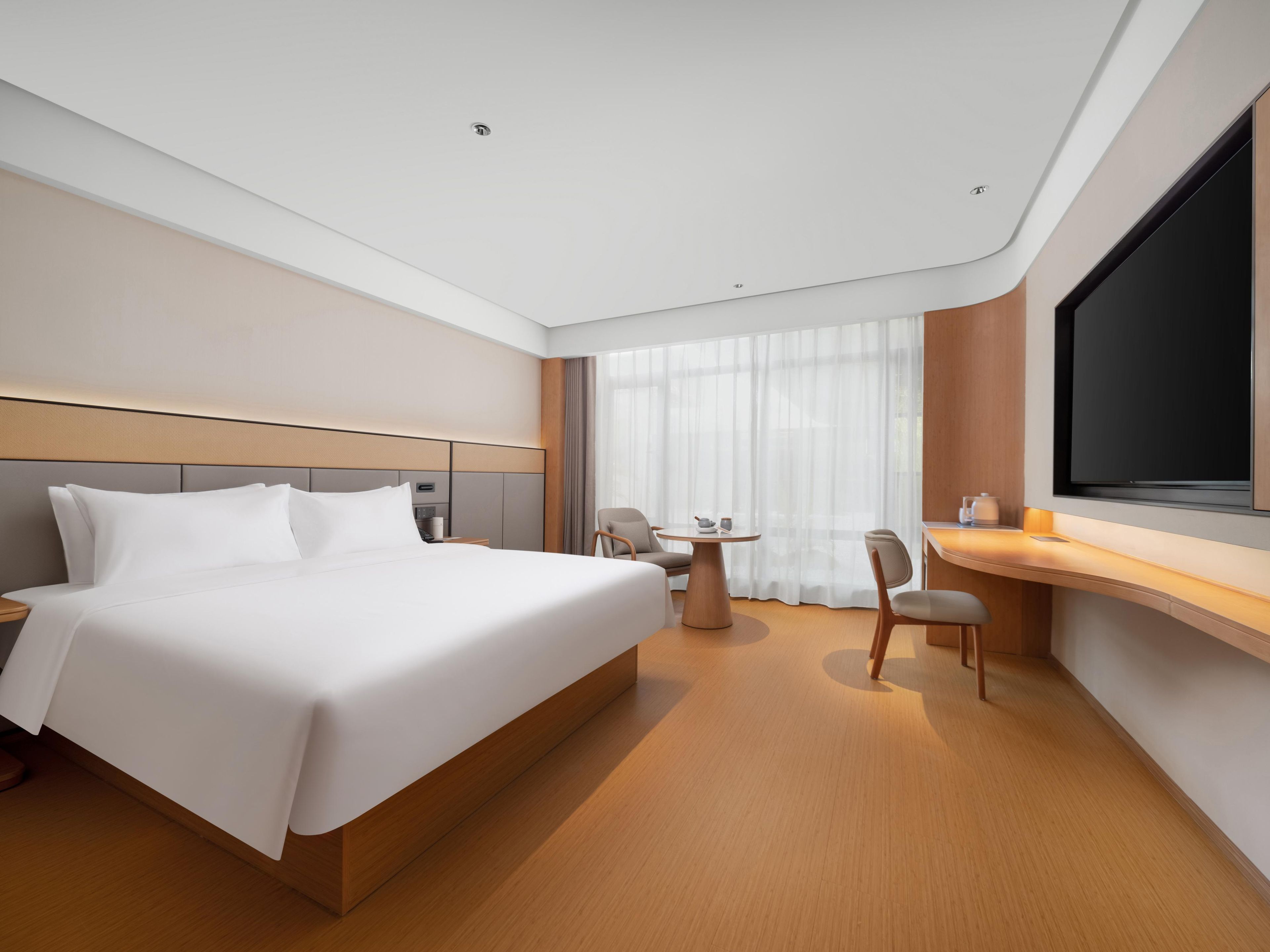 A modern hotel room with a large bed, a desk, and a TV.