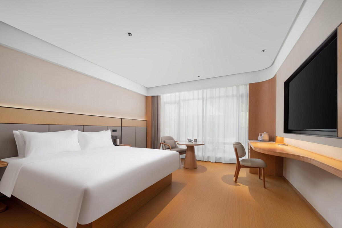 A modern hotel room with a large bed, a desk, and a TV.