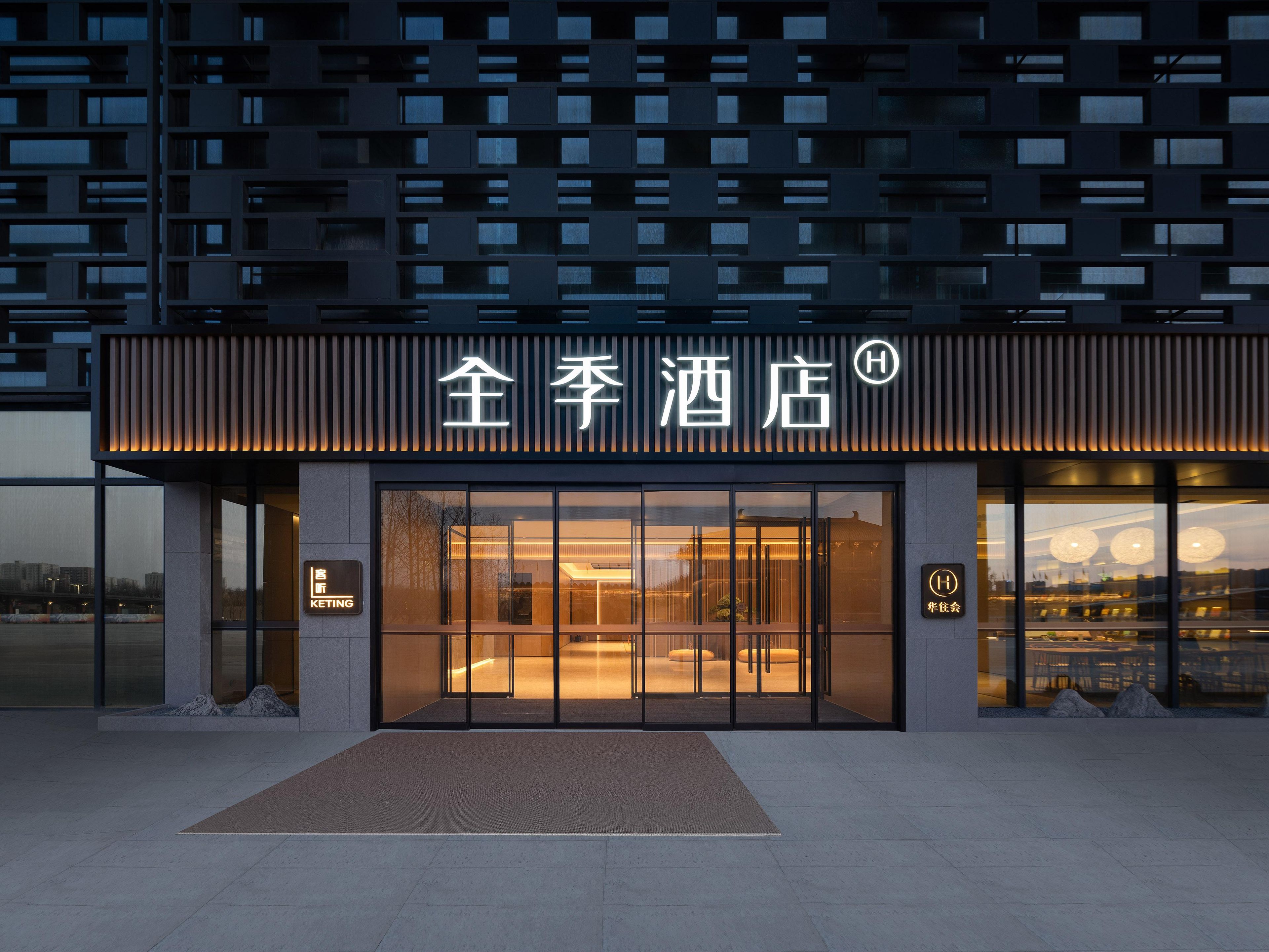 A hotel entrance with a modern facade, large glass doors, and a sign indicating a hotel.
