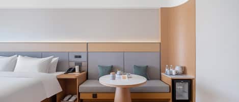 Una habitación de hotel moderna con cama, mesita de noche y un pequeño refrigerador.