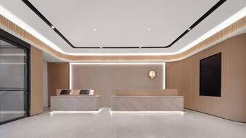 A modern reception area with a marble reception desk, a wall-mounted TV, and a ceiling with recessed lighting.
