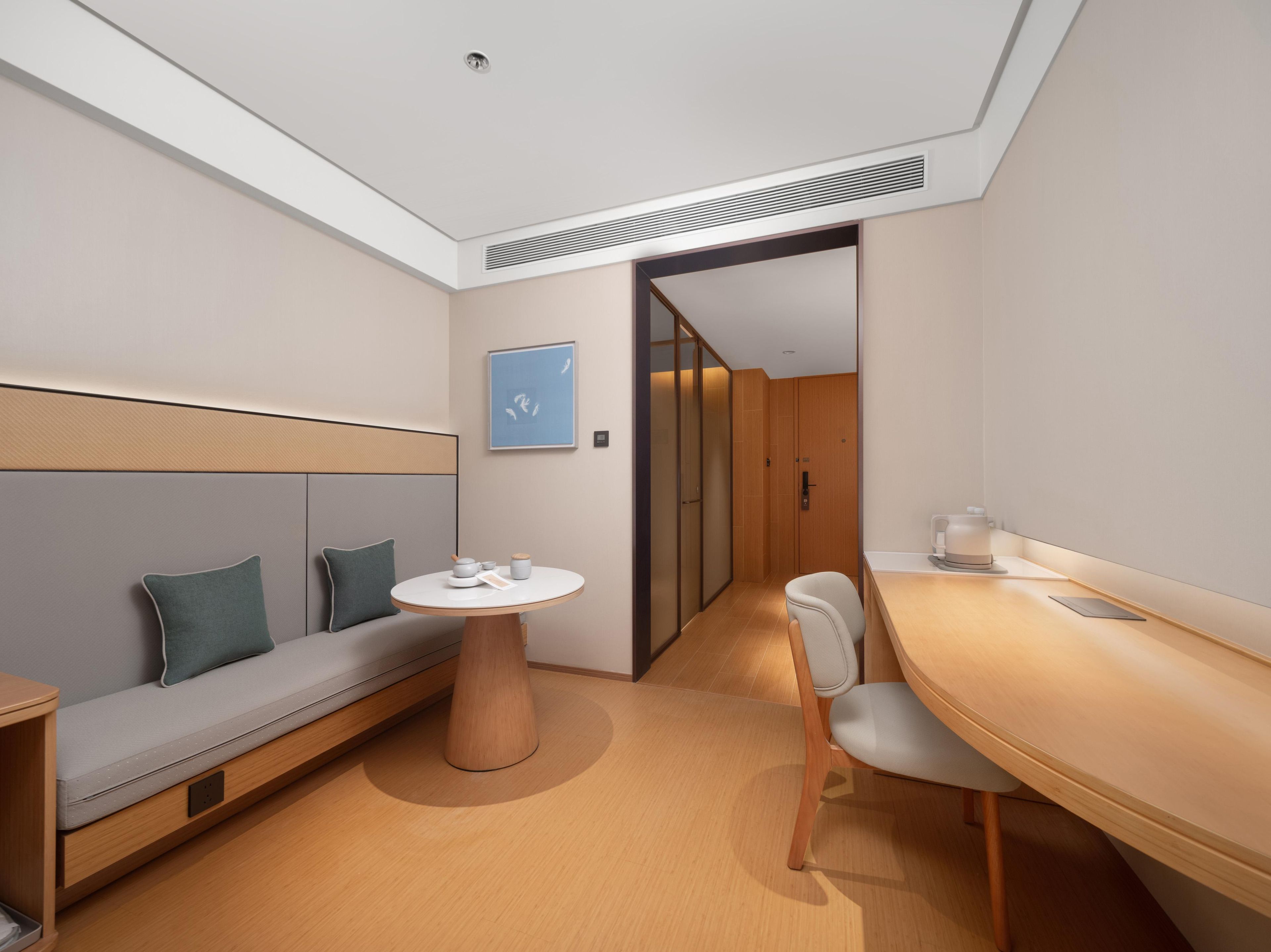 A modern hotel room with a sofa, a round table, a chair, and a wooden desk.