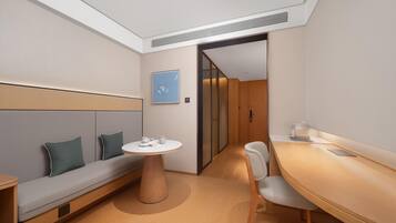 A modern hotel room with a sofa, a round table, a chair, and a wooden desk.