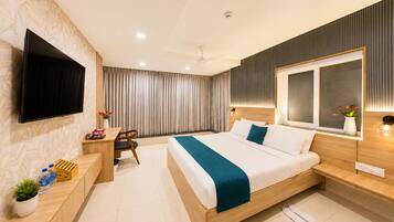 A modern hotel room with a large bed, a desk, a flat-screen TV, and a large window.