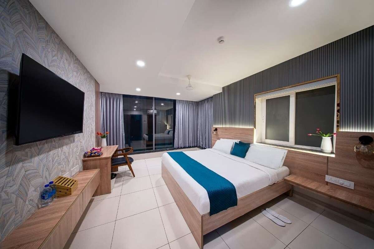 A modern hotel room with a large bed, a flat-screen TV, a desk, and a window with curtains.