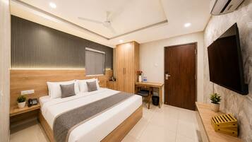A modern hotel room with a large bed, a desk, a flat-screen TV, and an air conditioning unit.