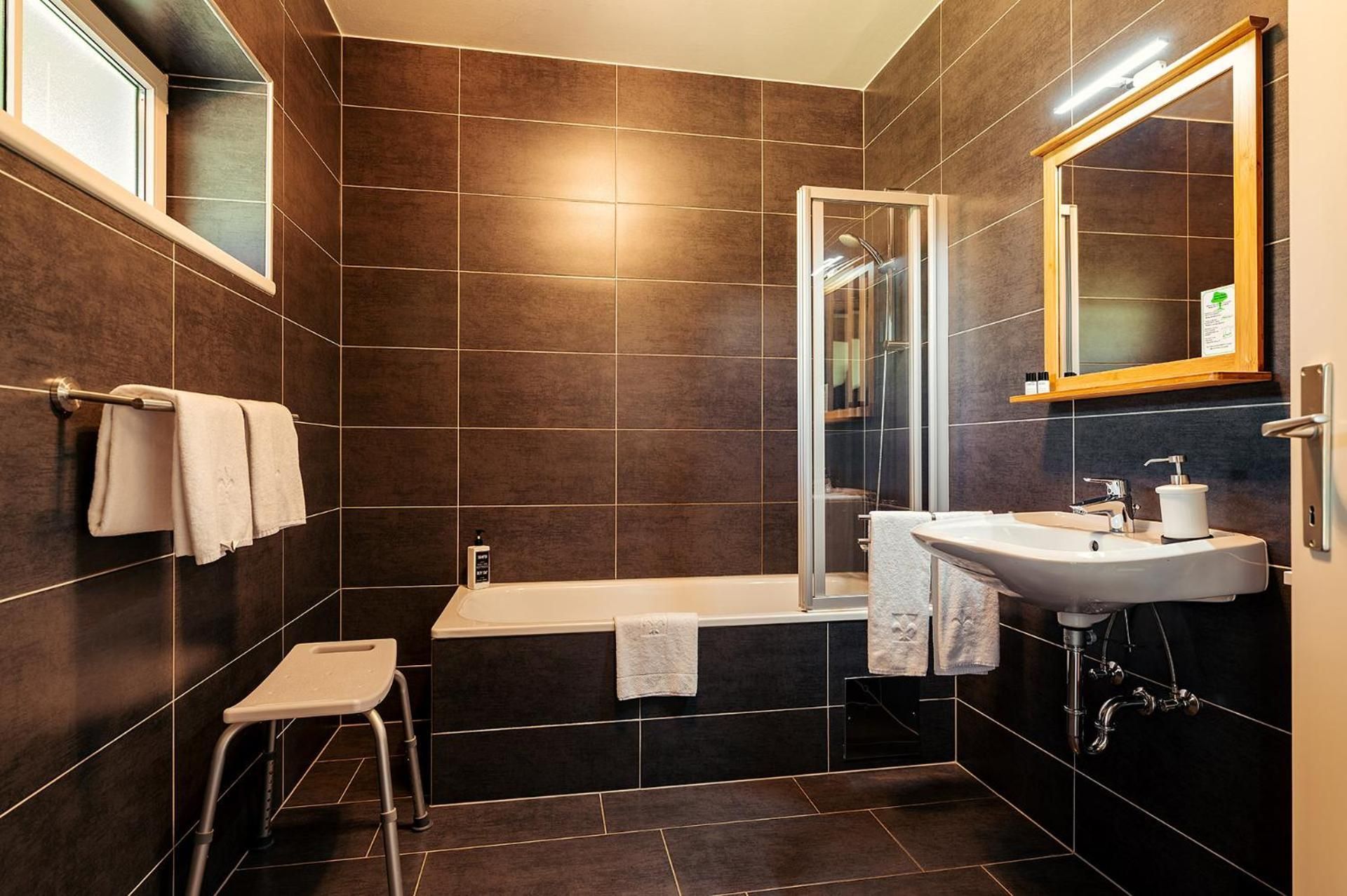 Ein modernes Badezimmer mit Badewanne, Duschkabine, Waschbecken und einem kleinen Hocker.