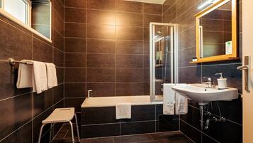 Ein modernes Badezimmer mit Badewanne, Duschkabine, Waschbecken und einem kleinen Hocker.