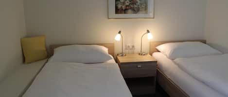 Une chambre d’hôtel avec deux lits simples, une table de chevet avec des lampes, un tableau au mur et un oreiller jaune.