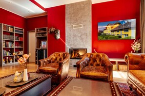 A room with red walls, a fireplace, leather armchairs, a bookshelf, and a painting of a house. - Gã¤stehaus Karl August (Fohnsdorf)