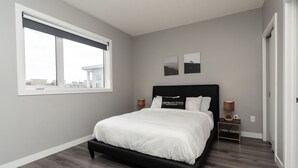 Un dormitorio moderno con una cama grande, una mesita de noche, dos lámparas de pared y un ventanal con vistas a edificios.