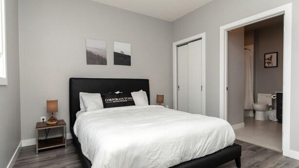 Un dormitorio moderno con una cama grande, una mesita de noche con lámpara, y una puerta que da a un baño.