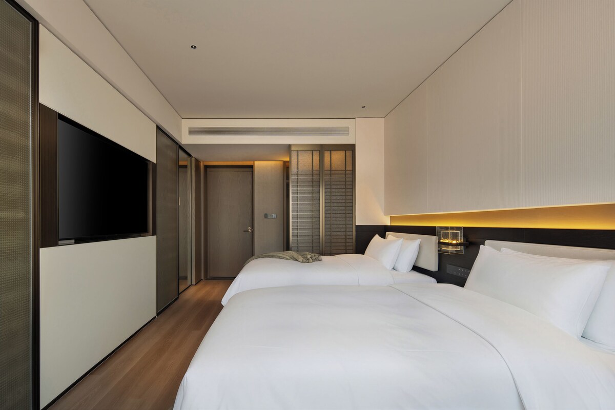 A hotel room with two beds, a TV, a wardrobe, and a large window.