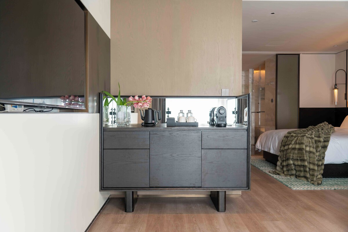 A modern hotel room with a grey cabinet, a bed with a blanket, and a shower area.