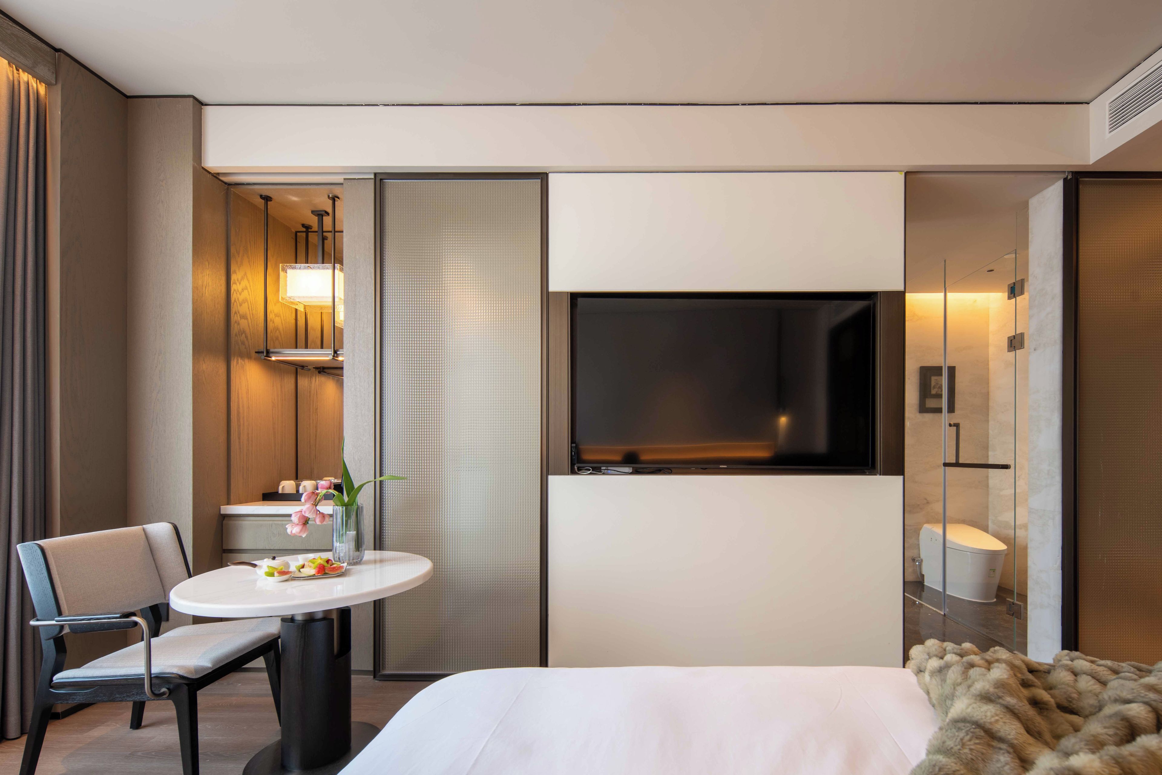 Habitación de hotel con una cama, una mesa redonda con sillas, un televisor montado en la pared y un baño visible a través de una puerta corredera.