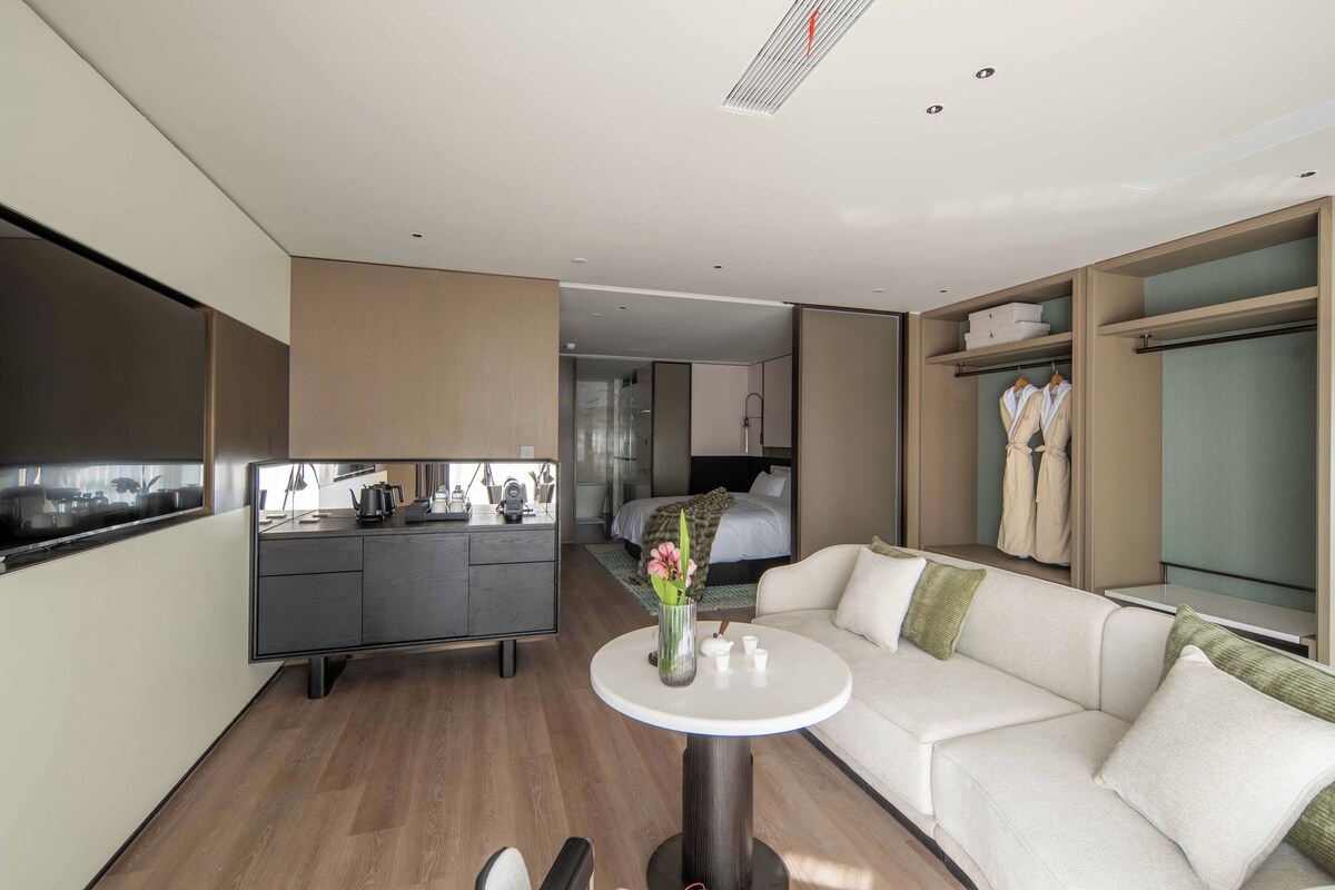 A modern hotel room with a kitchenette, a sofa, a small round table, and a walk-in closet.