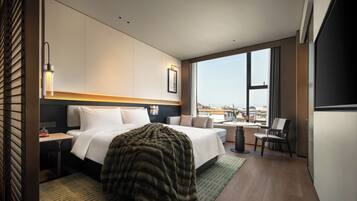 Habitación de hotel moderna con una cama grande, un escritorio, una silla y vistas de la ciudad a través de ventanas amplias.