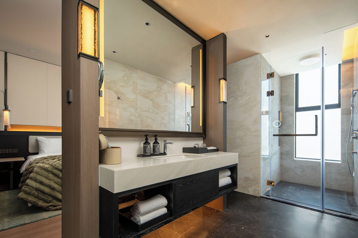 A modern bathroom with a large mirror, a white sink, and a glass shower enclosure.
