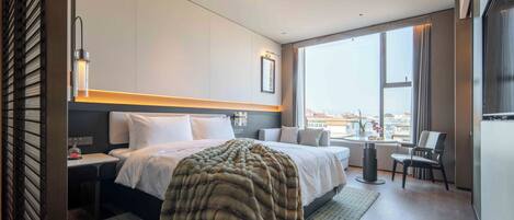 Habitación de hotel moderna con una cama grande, un escritorio, una silla y vistas de la ciudad a través de amplios ventanales.