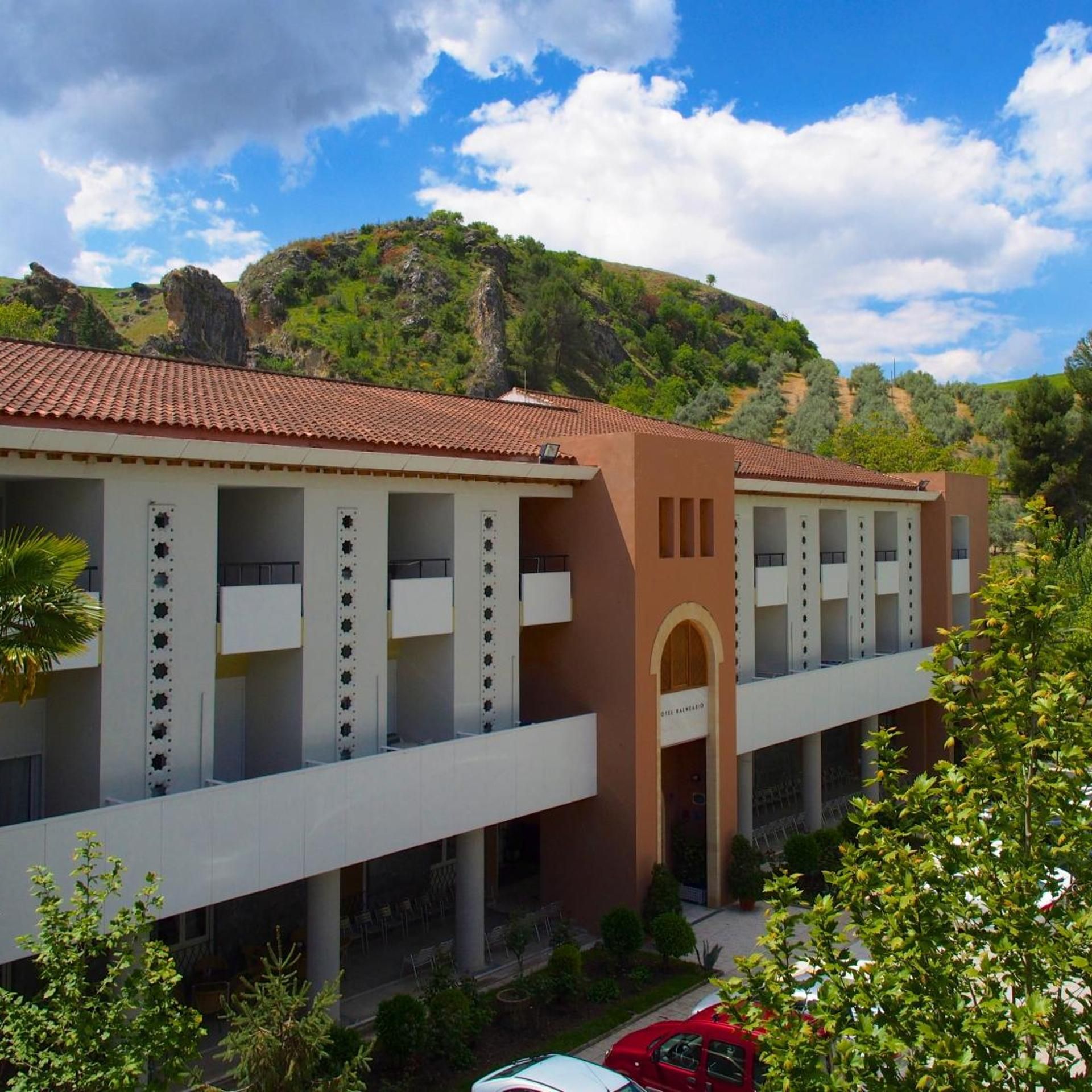 Un hotel con techo de tejas rojas, varios balcones y vistas a un paisaje montañoso.