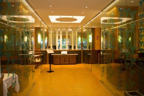 A reception area with a counter, seating, and glass walls with a leaf pattern. - Balneario De Alhama De Granada (Alhama de Granada)
