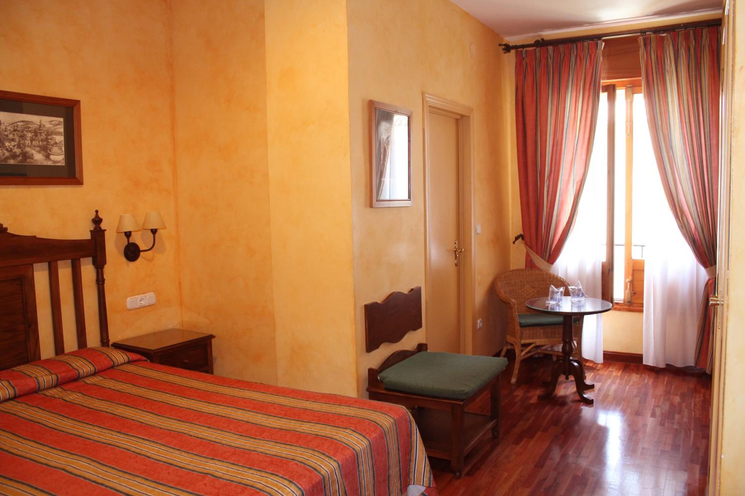 Una habitación de hotel con cama, una silla, una mesita y una ventana con cortinas.