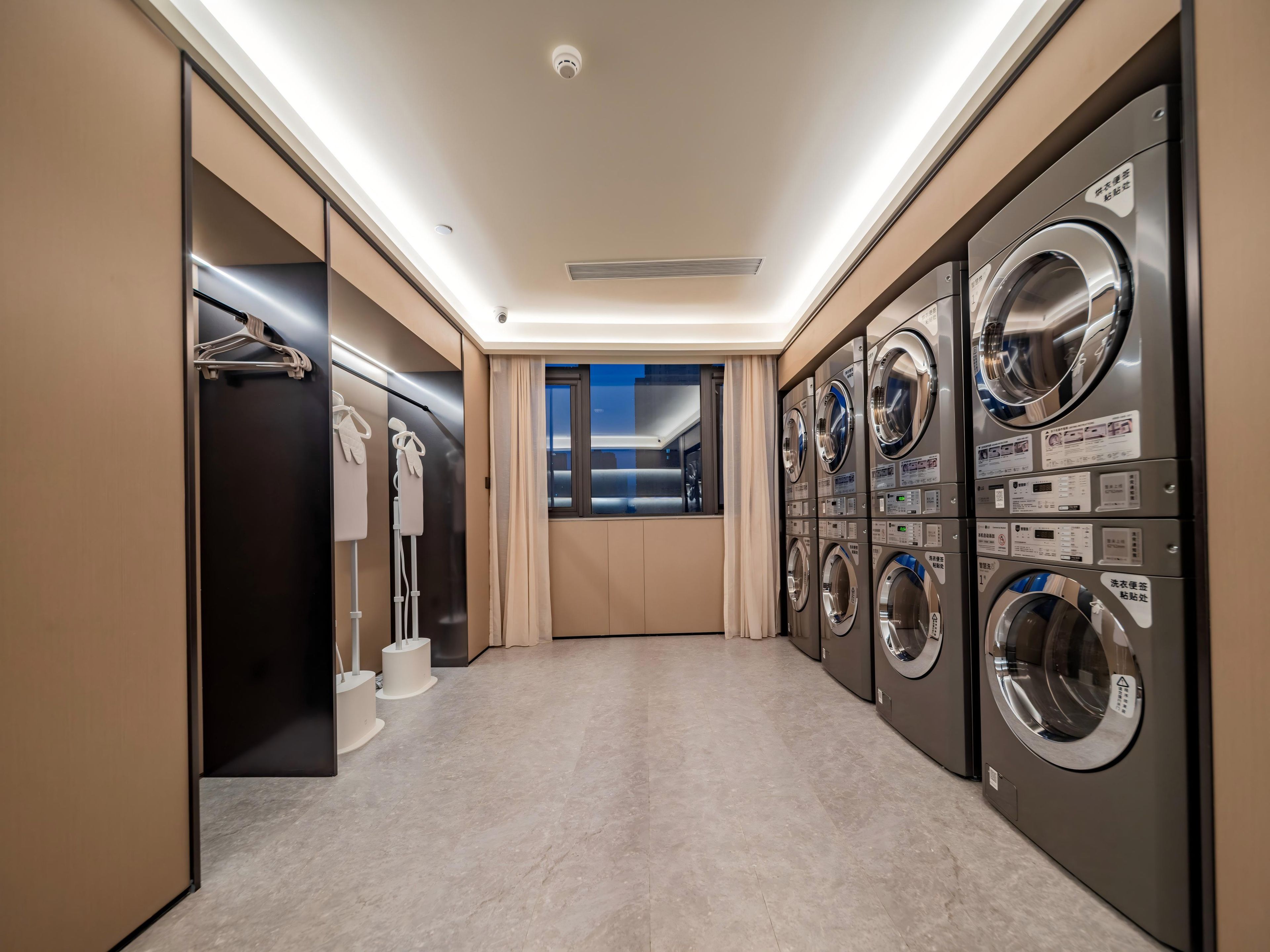 A laundry room with multiple washing machines, a drying rack, and a mirror.
