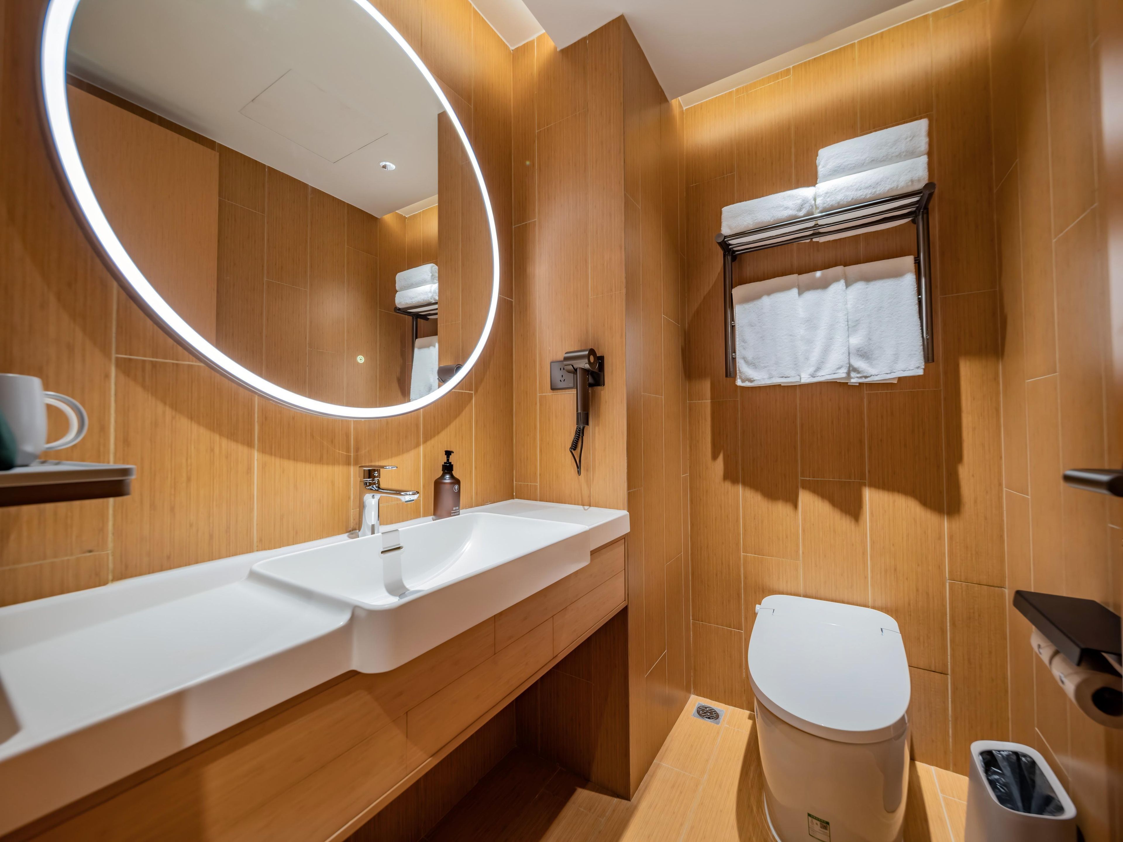 A modern bathroom with a wooden finish, a white sink, a toilet, and a towel rack.