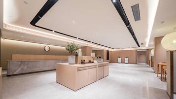 A modern hotel lobby with a reception desk, seating area, and a large plant centerpiece.
