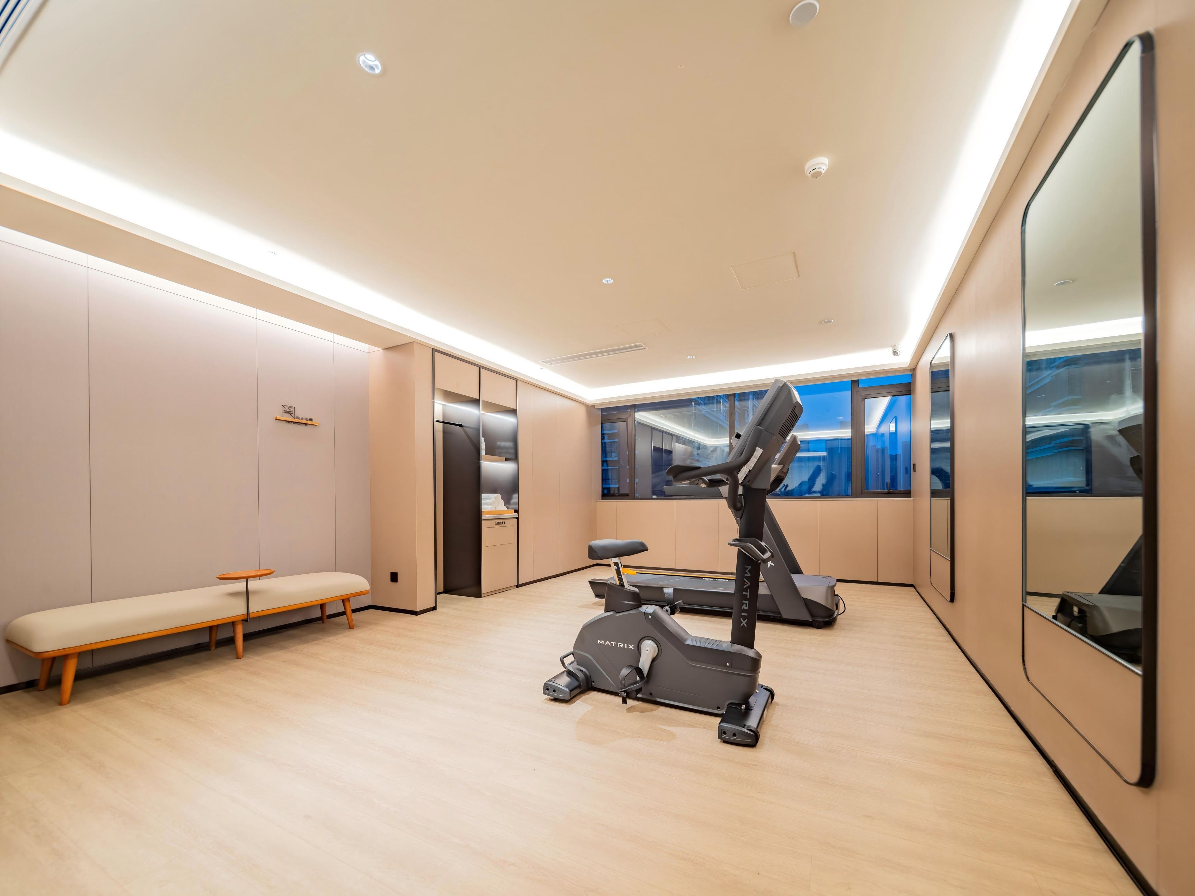A modern fitness room with a treadmill, a bench, and a mirrored wall.