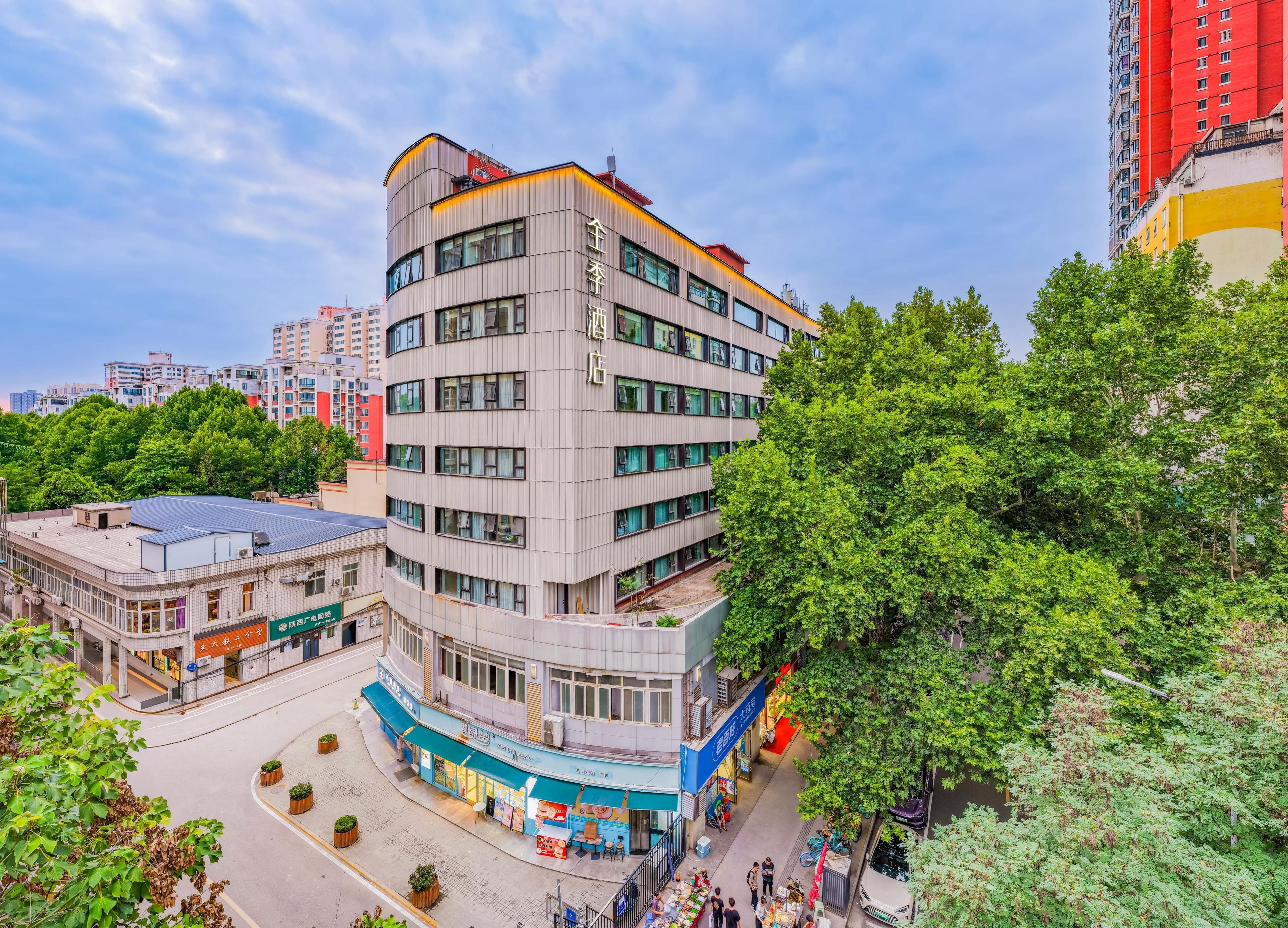 A multi-story building with a curved facade, surrounded by greenery and other buildings.