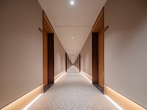 Ein langer, schmaler Hotelkorridor mit einem gemusterten Boden und eingelassener Beleuchtung.