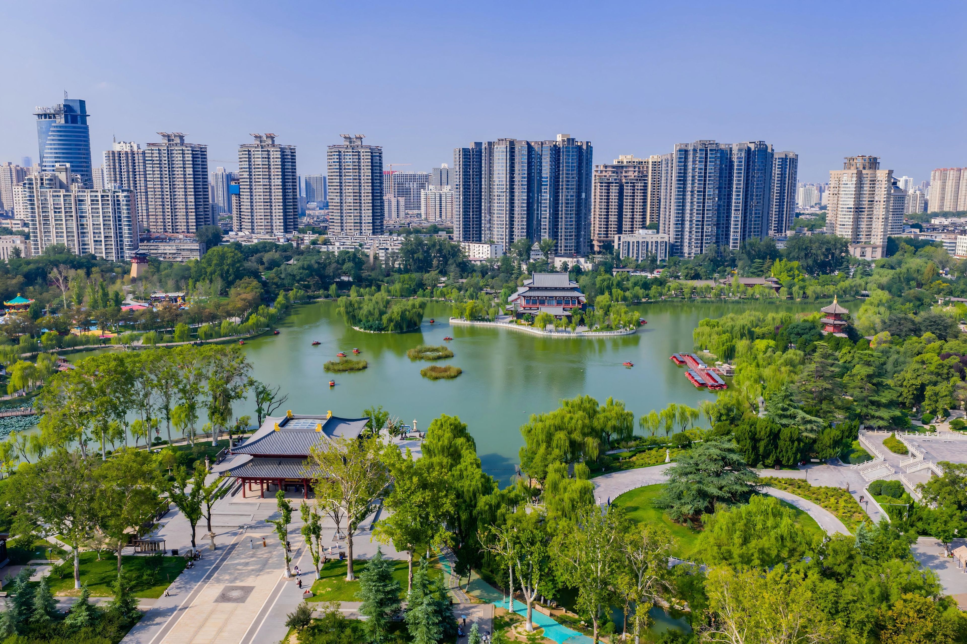 A park with a lake, surrounded by trees and a traditional building.