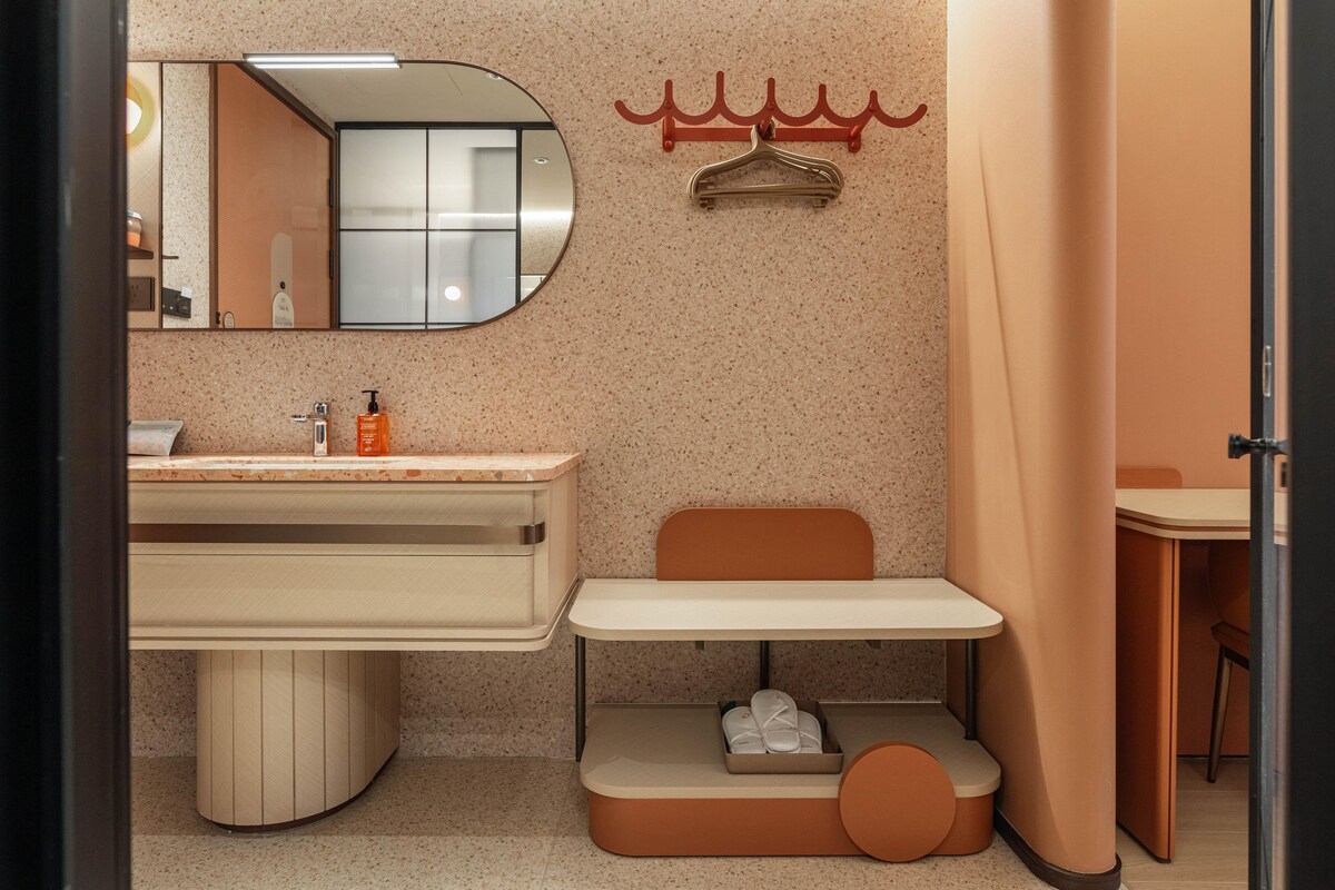 Ein modernes Badezimmer mit Waschtisch, Spiegel, Handtuchhalter und einer kleinen Sitzecke mit Hausschuhen.