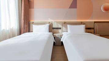 A hotel room with two single beds, a nightstand, a wall-mounted control panel, and a large window with curtains.