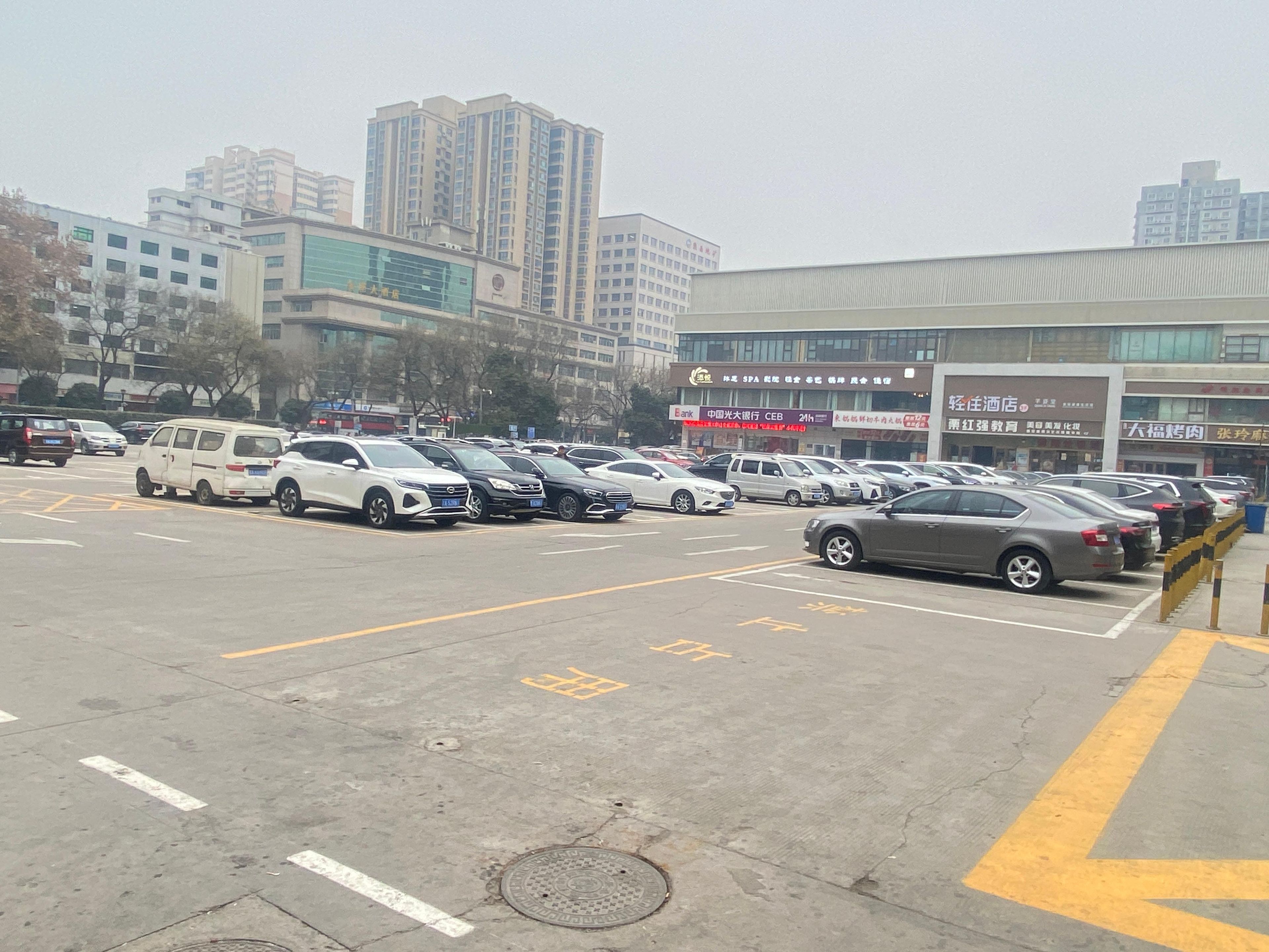 A parking lot with multiple cars, a building with signage, and a cityscape in the background.