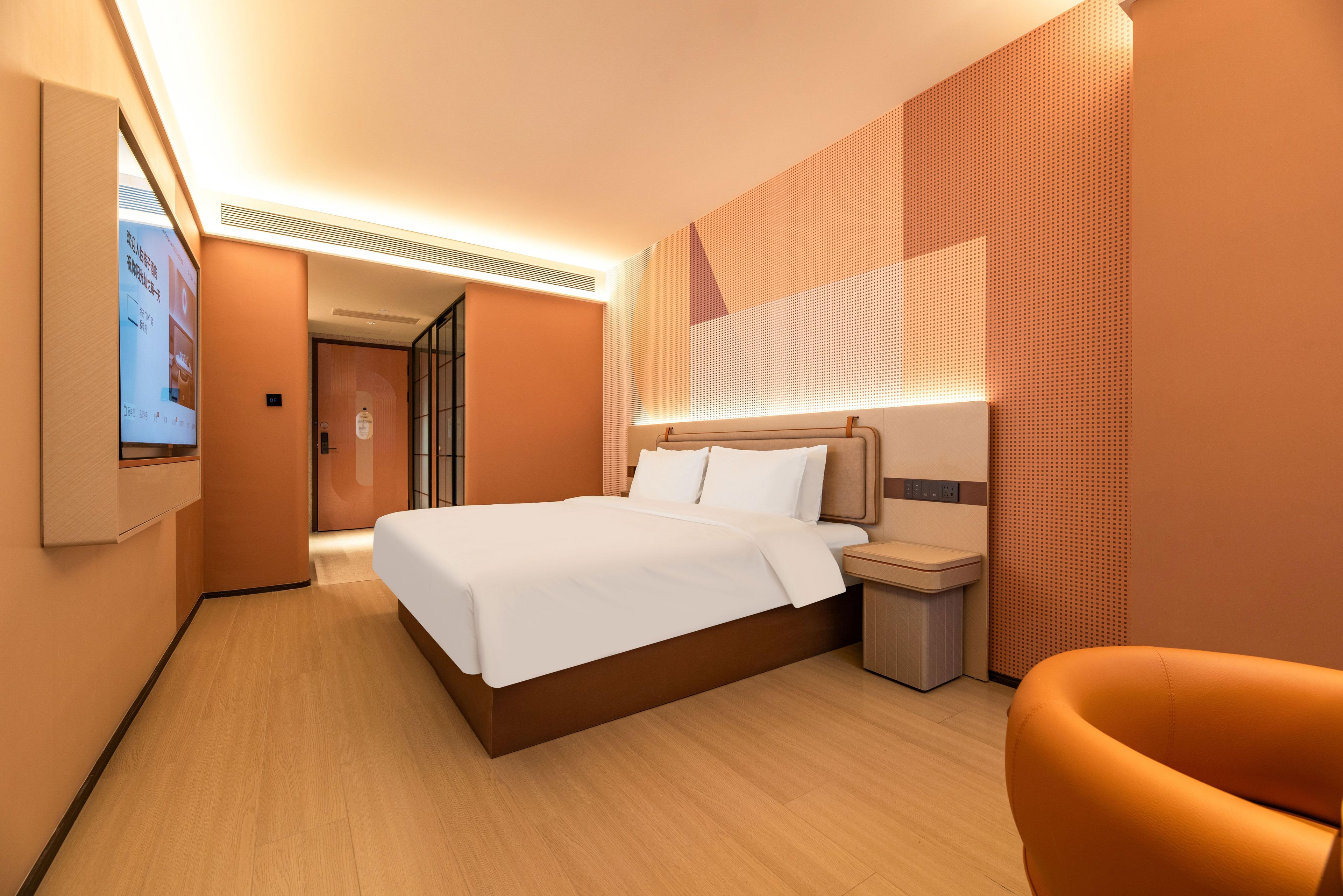 A hotel room with a bed, bedside table, chair, and a large window with blinds.