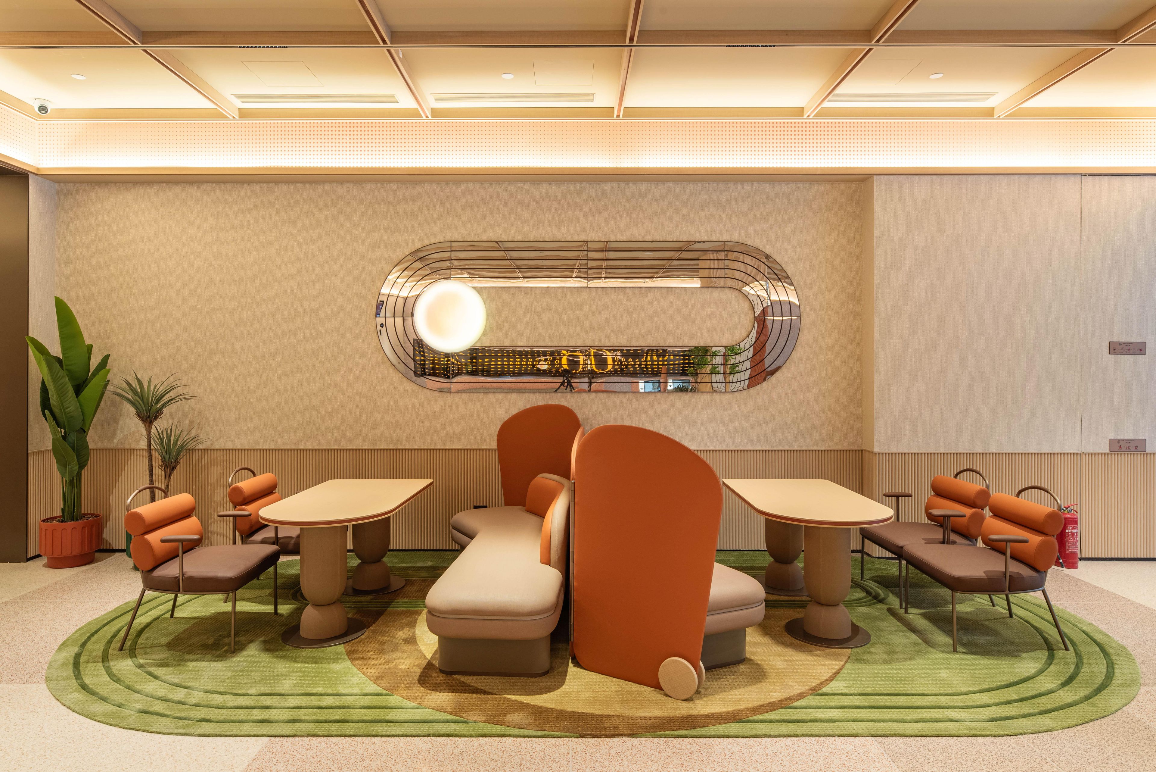 A modern interior with a seating area featuring round tables and cushioned chairs, a decorative wall with a circular mirror, and potted plants.