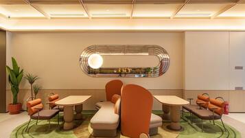 A modern interior with a seating area featuring round tables and cushioned chairs, a decorative wall with a circular mirror, and potted plants.